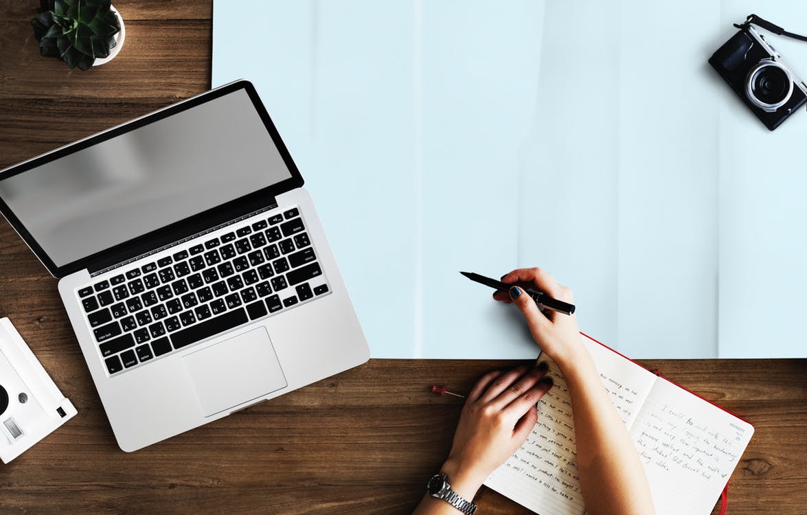 Woman with laptop writing on journal