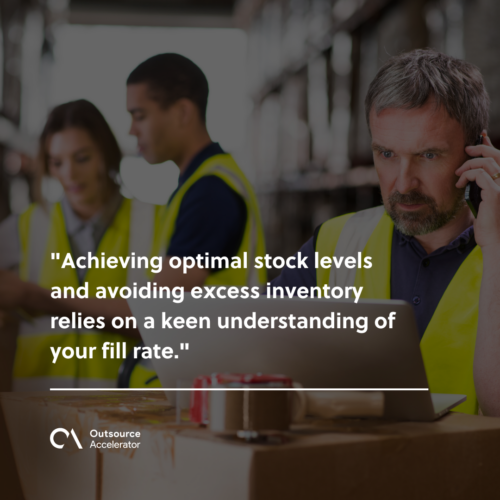 a mature warehouse manager stands in his warehouse looking at his laptop whilst talking on the telephone