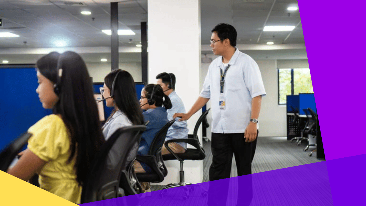 Row of call center agents in headsets at workstations with a supervisor standing beside them in a Philippine office.