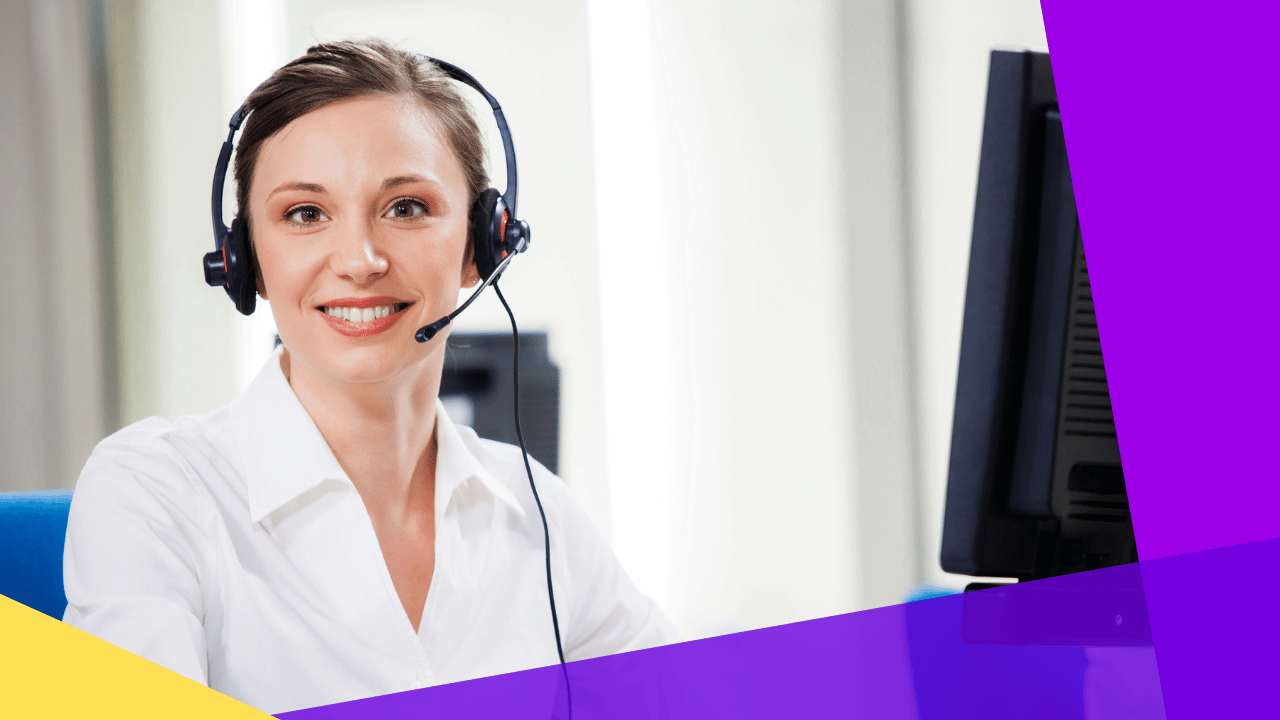 Smiling customer support agent in a headset and white blouse seated beside a computer monitor, bright office light.